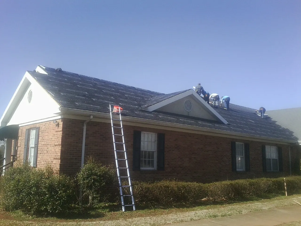 Crew tearing shingles off a brick ranch roof with a ladder set — Metal Roof Repair work by our crew in Frazeysburg