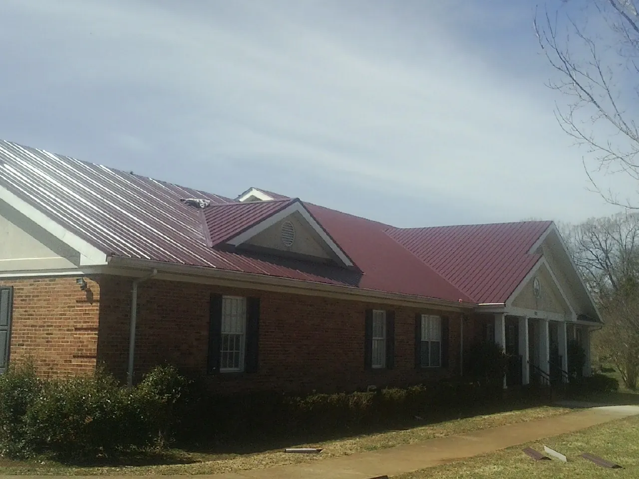Red metal roof with gabled entries on a long brick building, from a Hail Damage Roof Repair job in Frazeysburg