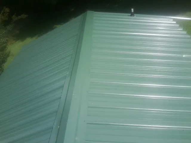 New green metal panels meeting at the ridge of a roof — Flat Roof Repair work by our crew in Frazeysburg