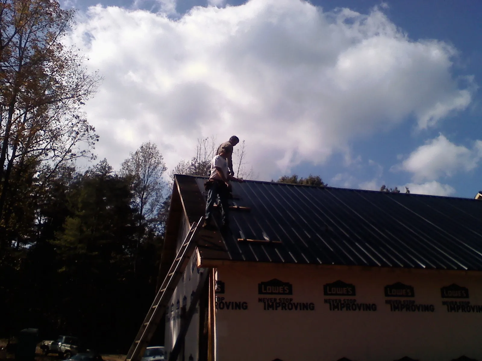 Roofer fastening dark metal panels high against a cloudy sky, from a Roof Inspection job in Frazeysburg