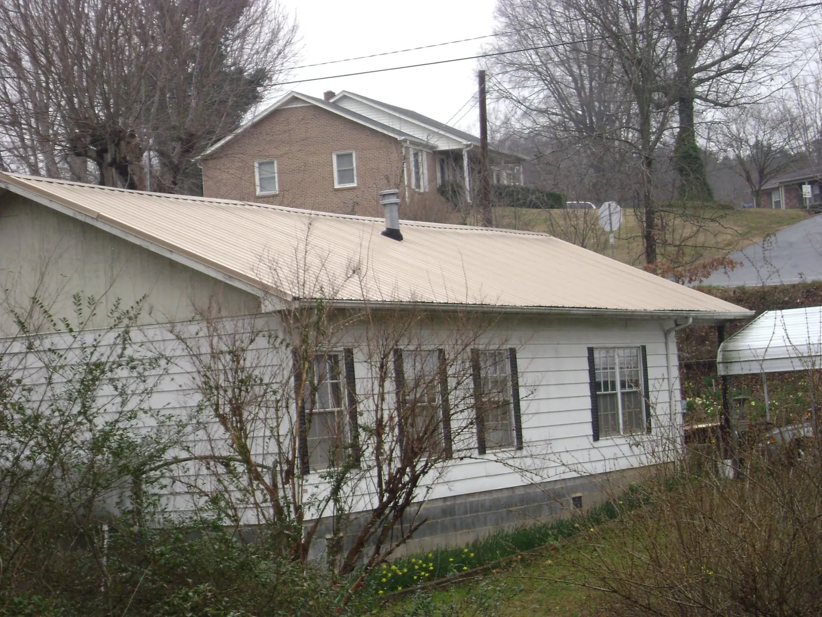 Tan metal roof on a white sided house set into a hillside — Commercial Roofing by Roofing Brothers in Frazeysburg